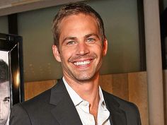 a smiling man in a suit and white shirt next to a framed photo with a movie poster on it