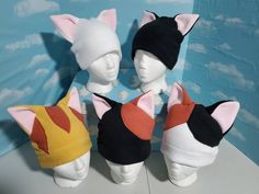 four stuffed cats wearing hats on top of a white table next to a blue wall