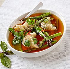 a bowl of soup with asparagus and dumplings on a white placemat