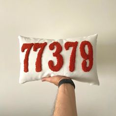 a person holding up a pillow with the number 739 on it in red and white