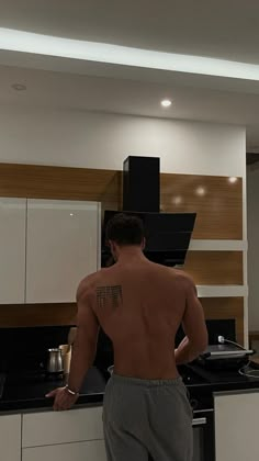 a man with no shirt on standing in front of a stove top oven and cabinets