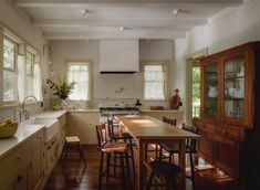 a large kitchen with wooden floors and white walls, along with an island table surrounded by bar stools