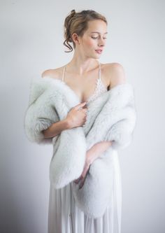 a woman in a white dress is holding a fur shawl over her shoulder and looking down at the ground