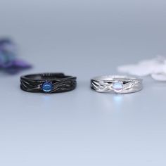 two wedding bands with blue stones are on a table next to some purple and white flowers