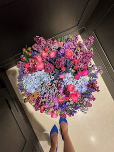 a woman's feet are standing in front of a bouquet of purple and blue flowers