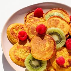 a white plate topped with pancakes covered in kiwis and raspberry slices