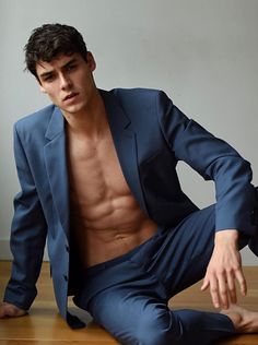 a shirtless man in a blue suit sitting on the floor with his legs crossed