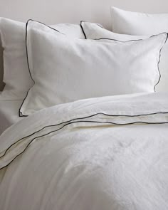 a bed with white sheets and black piping on the pillowcase, along with two pillows