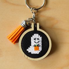 a cross stitch keychain with a halloween ghost on it's front and an orange tassel hanging from the back