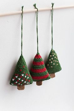 three small knitted christmas trees hanging from a hook on a white wall with green cord