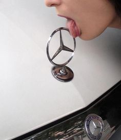 a woman sticking her tongue out while standing next to a mercedes logo on a car