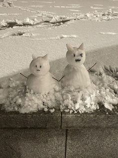 two snowmen sitting in the middle of a pile of snow with their heads turned to look like cats