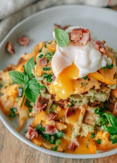 a white plate topped with lasagna covered in cheese and bacon next to green leafy garnish