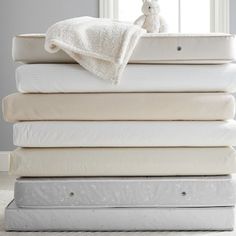 a stack of mattresses and blankets with a stuffed animal on the top, in front of a window