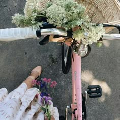 a pink bicycle with flowers in the basket and someone's feet on the ground