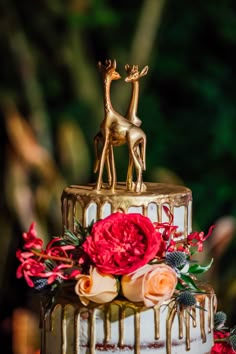 a wedding cake decorated with flowers and gold giraffe figurines on top