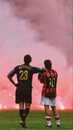 two soccer players are standing on the field as fireworks go off in the sky behind them