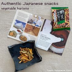 an open japanese snack book next to a bowl of fried vegetables and crackers on a table