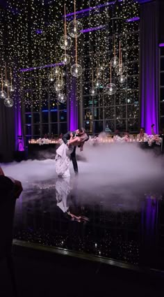 two people are dancing in the middle of a foggy dance floor with chandeliers hanging from the ceiling