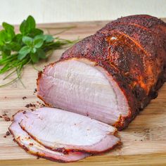 sliced ham sitting on top of a wooden cutting board next to fresh herbs and leaves