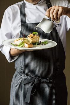 a man in an apron is pouring sauce on a plate with food and garnishes