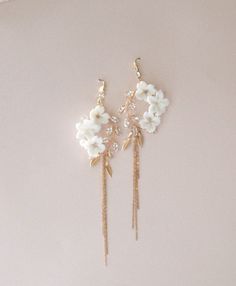 two white flowers are hanging from the side of a pair of gold - tone earrings