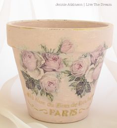 a pink flower pot with roses painted on the side and words written in gold lettering