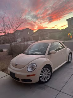 a beige car parked in front of a house at sunset with the sun going down