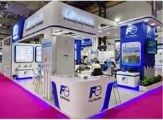 a trade show booth with purple carpet and blue lighting on the walls, while people are sitting at tables in front of it