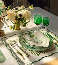 the table is set with green and white plates, silverware, and flowers in vases