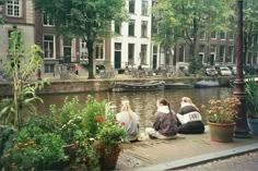 three women sitting on the edge of a canal