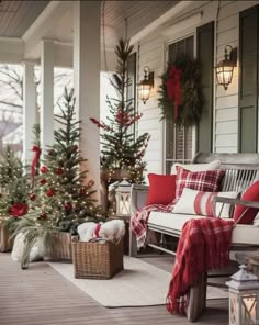 the porch is decorated for christmas with red and white pillows, plaid throwers, evergreen trees, and lanterns