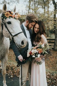 a bride and groom standing next to a horse with flowers in their hair, holding the bridals