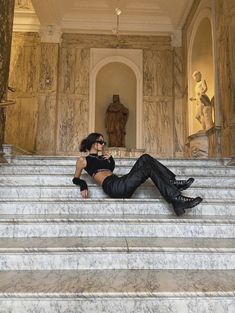 a woman sitting on the steps of a building with her legs crossed and wearing black boots