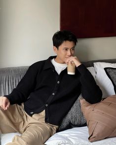 a man sitting on top of a bed holding a coffee cup in his hand and looking at the camera