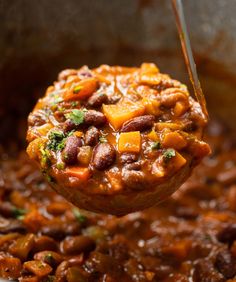 a spoon full of beans and vegetables being lifted from a pot