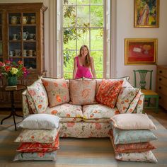 a woman sitting on top of a couch in front of a window with lots of pillows