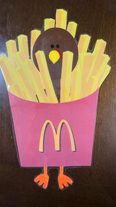 a paper cut out of a turkey and french fries in a pink container on a wooden table