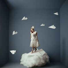 a woman standing on top of a cloud with paper airplanes in the air above her