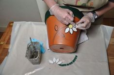 a person in white gloves is decorating an orange flower pot with flowers on it