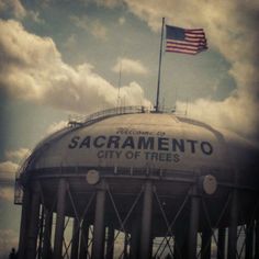 an old water tank with the american flag flying above it and some clouds in the background