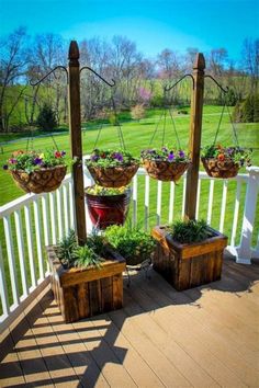 an outdoor deck with potted plants and hanging planters on the posts, in front of a green field