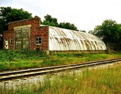 an old rusted out building sitting on the side of train tracks next to trees