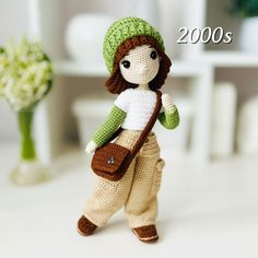 a crocheted doll with a green hat and brown purse is standing in front of a white table