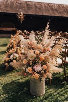 an arrangement of flowers in a vase on the grass at a wedding ceremony with chairs