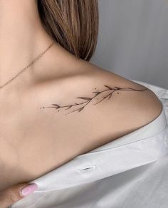 the back of a woman's shoulder with a small branch tattoo on her left shoulder