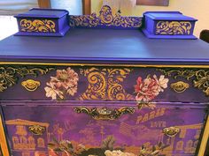 a purple and gold painted dresser with flowers on it