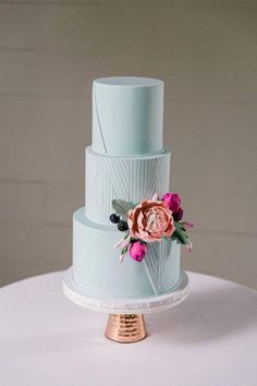 a three tiered blue cake with pink flowers on top