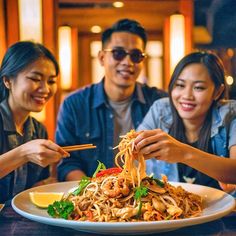 three people eating noodles with chopsticks at a restaurant