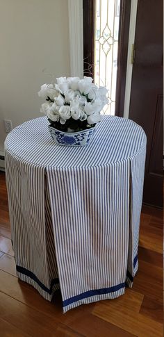 a blue and white striped table cloth with flowers in a vase on it sitting on top of a wooden floor